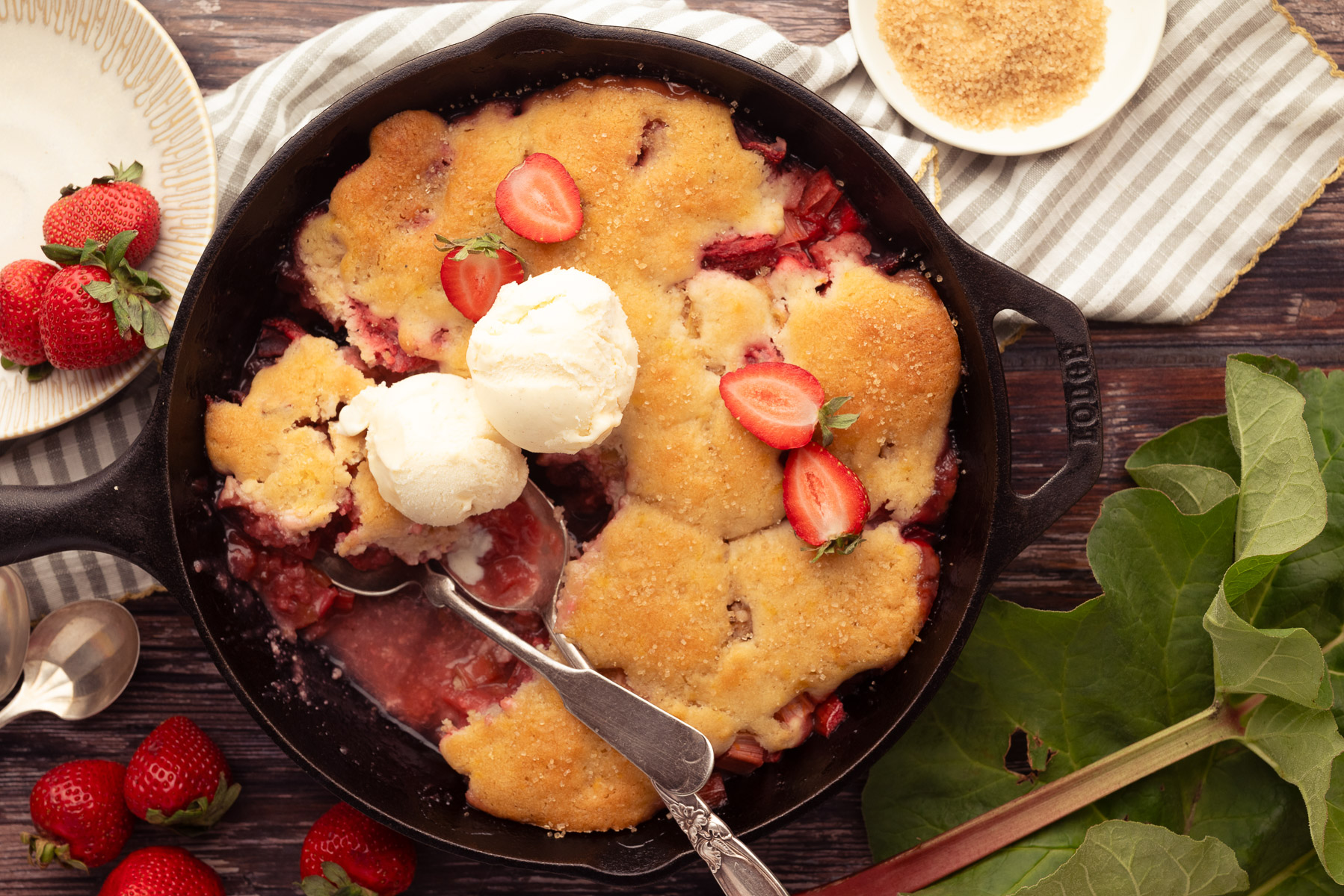 Overhead view of strawberry rhubarb cobbler in a cast iron skillet with vanilla ice cream