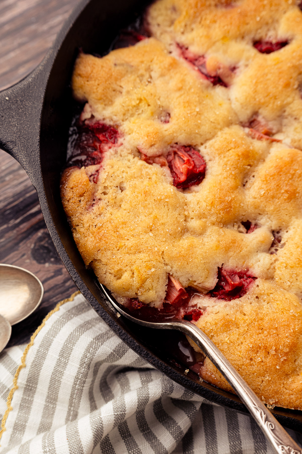 Close-up of golden cobbler topping in a cast iron skillet showing fruit bubbling through