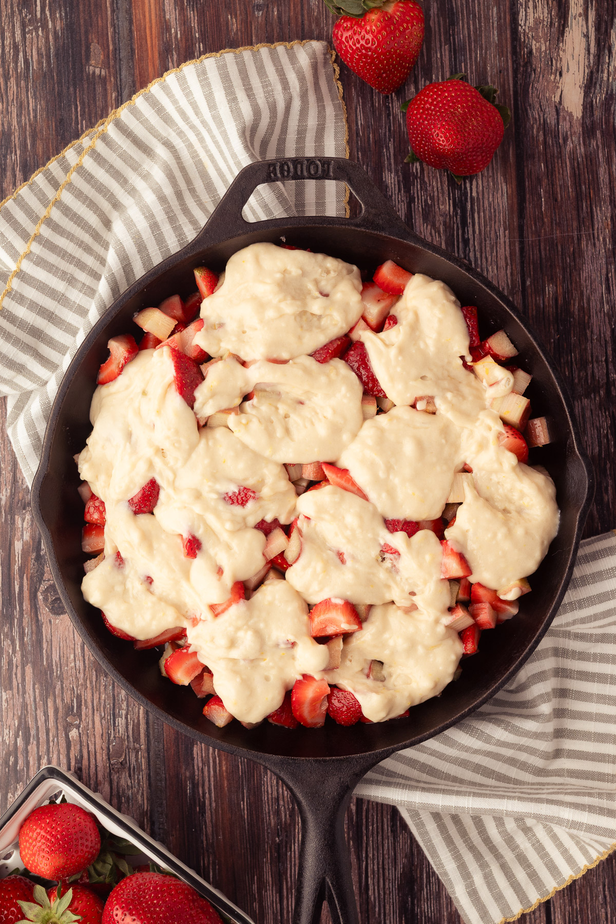 Cobbler batter dolloped over strawberry rhubarb filling in a cast iron skillet