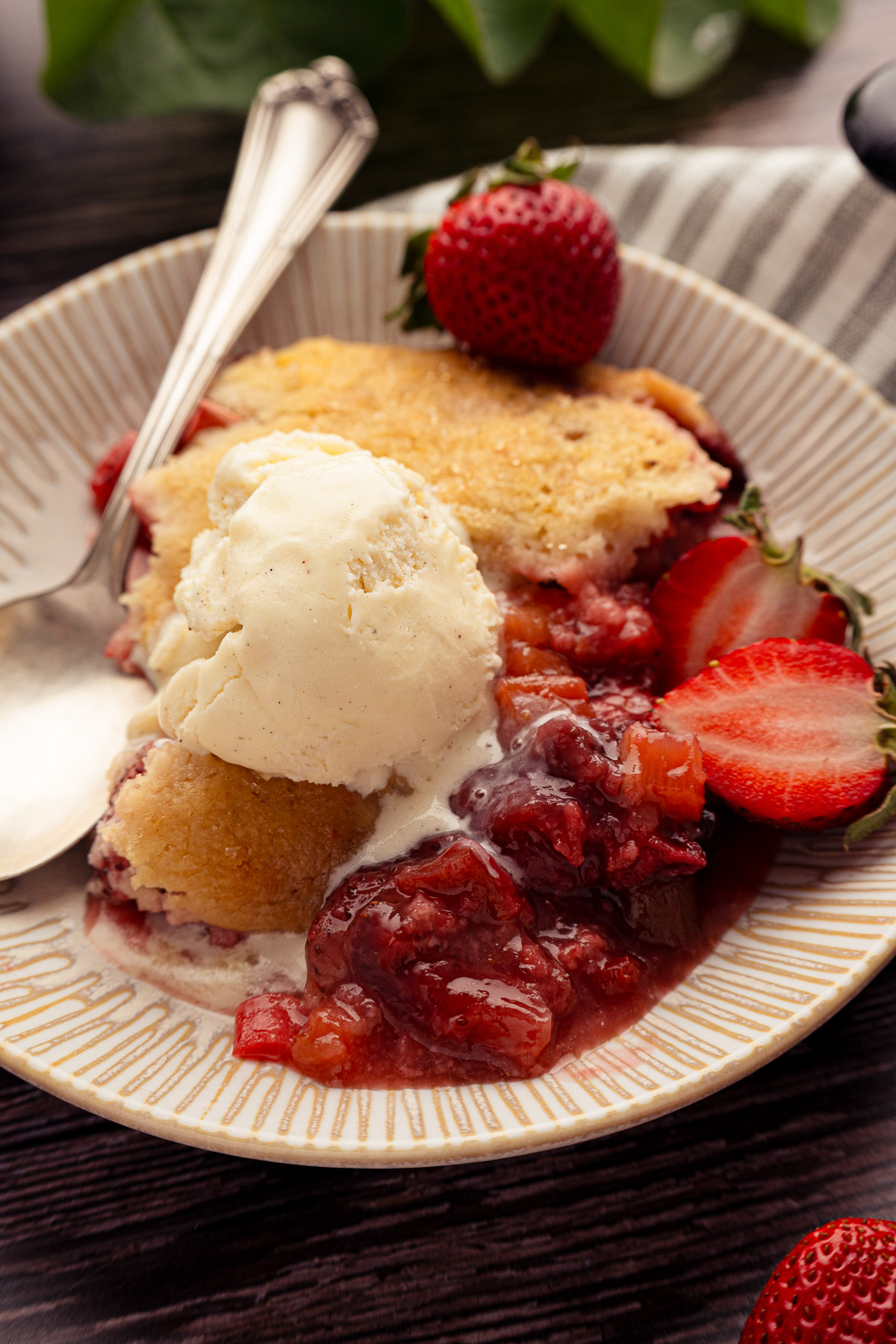 Serving of strawberry rhubarb cobbler on a plate with vanilla ice cream
