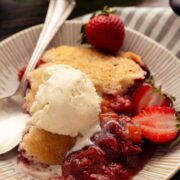 Strawberry rhubarb cobbler served on a plate with vanilla ice cream and fresh strawberries