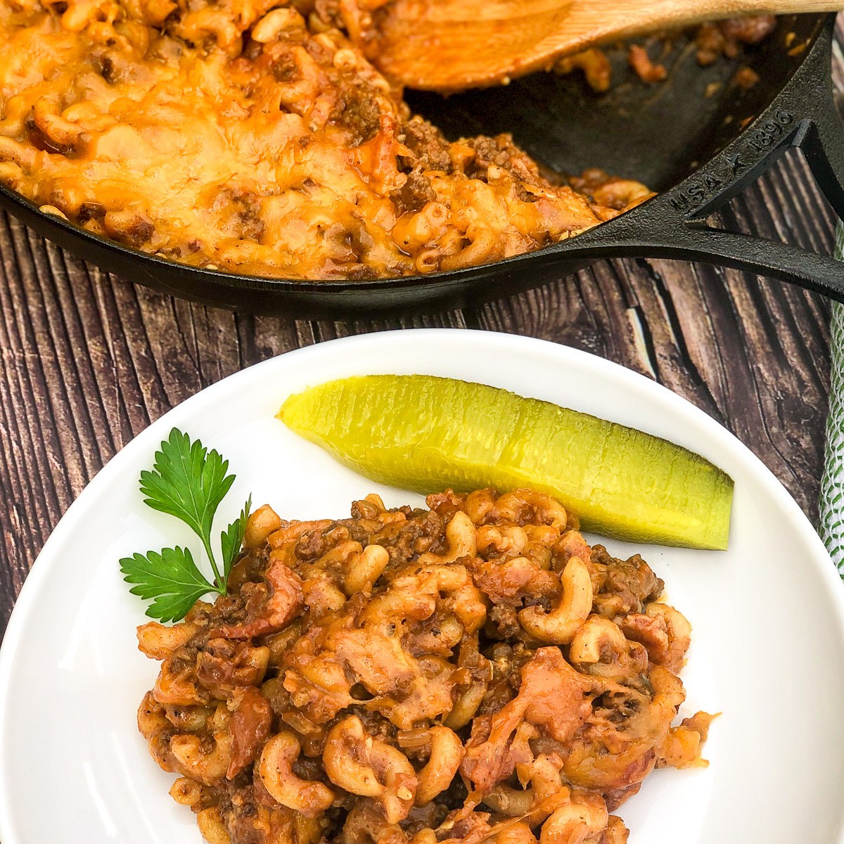 A plate of bacon cheeseburger casserole served with a dill pickle spear.