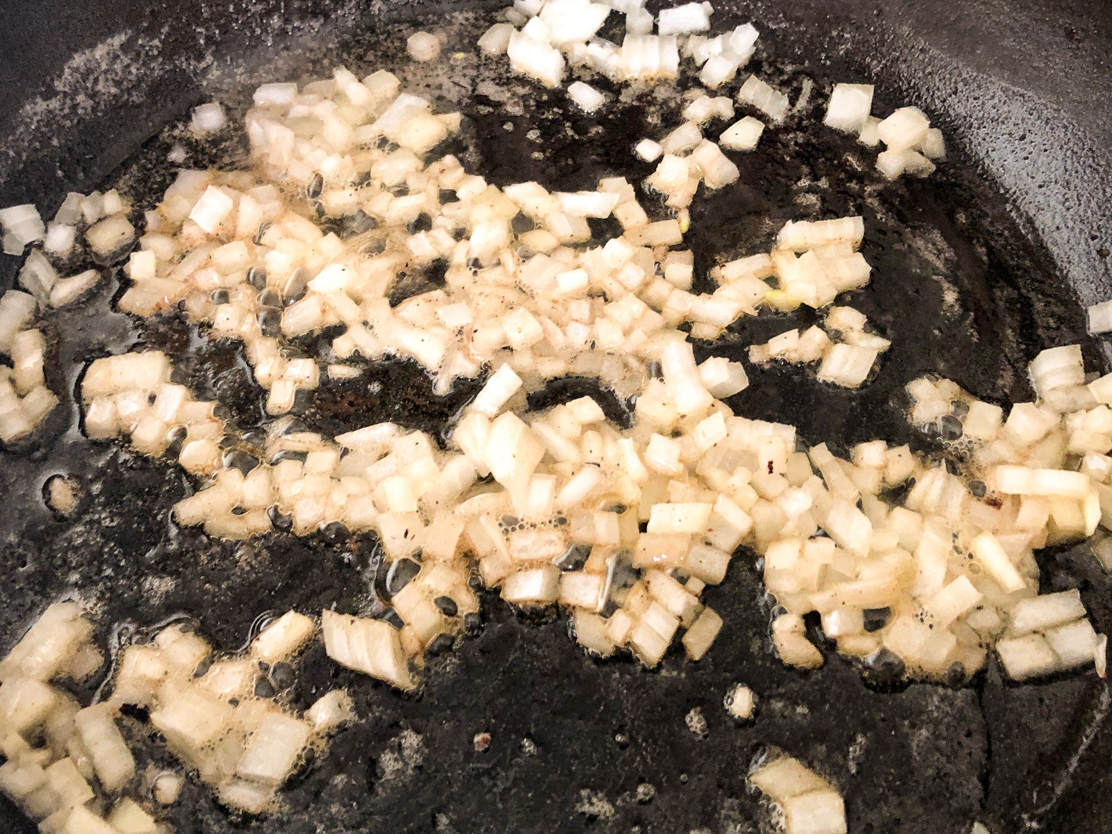 Diced onion cooking in bacon fat in a cast iron skillet.