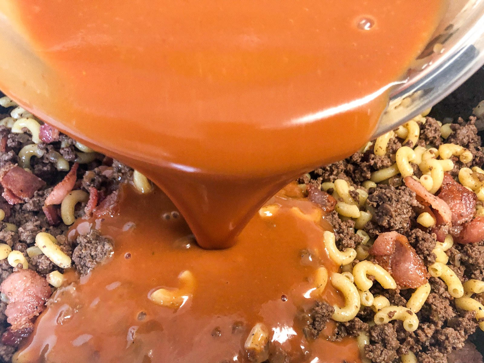 Pouring the tangy cheeseburger sauce into the beef mixture.