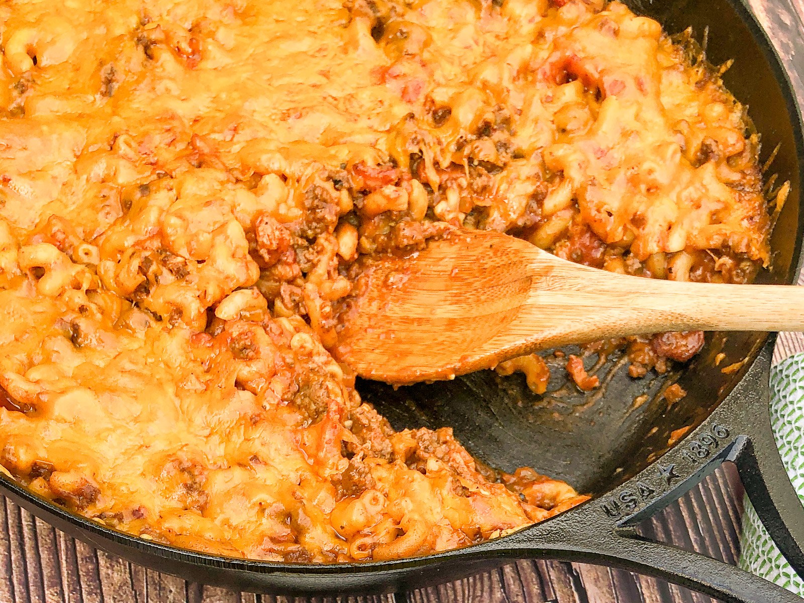 Stirring the finished bacon cheeseburger casserole in a cast iron skillet.