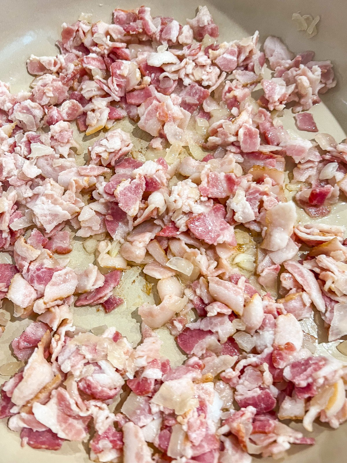 Chopped bacon and diced onion cooking in a cast iron skillet.