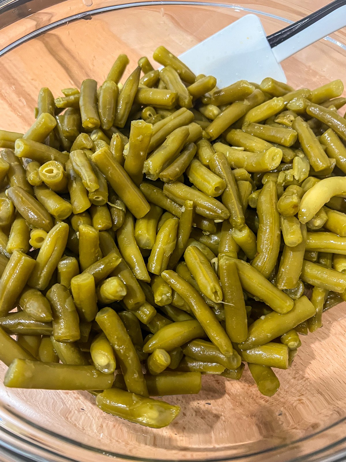 Drained canned green beans in a glass mixing bowl.
