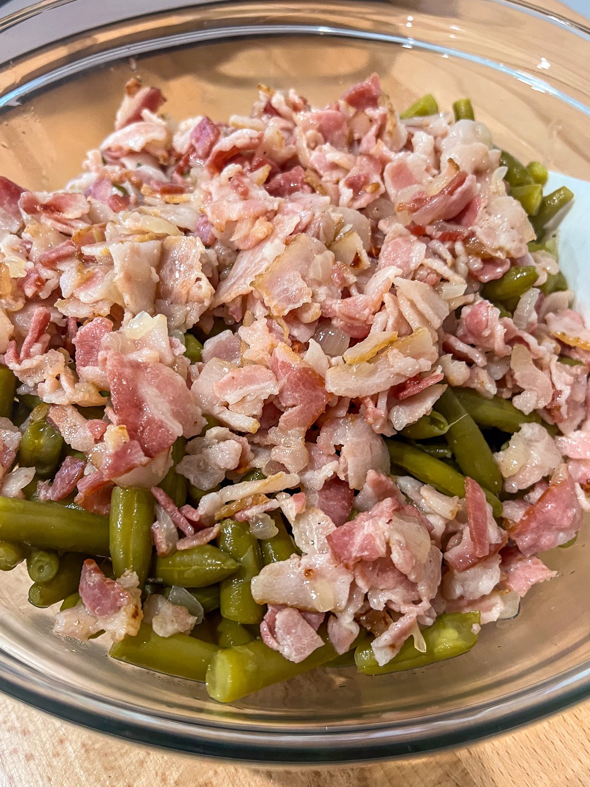 Cooked bacon and onion added to a bowl of drained green beans.