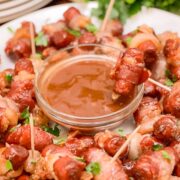 Bacon wrapped smokies arranged around BBQ sauce on a white platter.