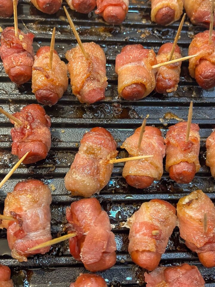 Brown sugar bacon wrapped smokies crisping on a cast iron grill grate.