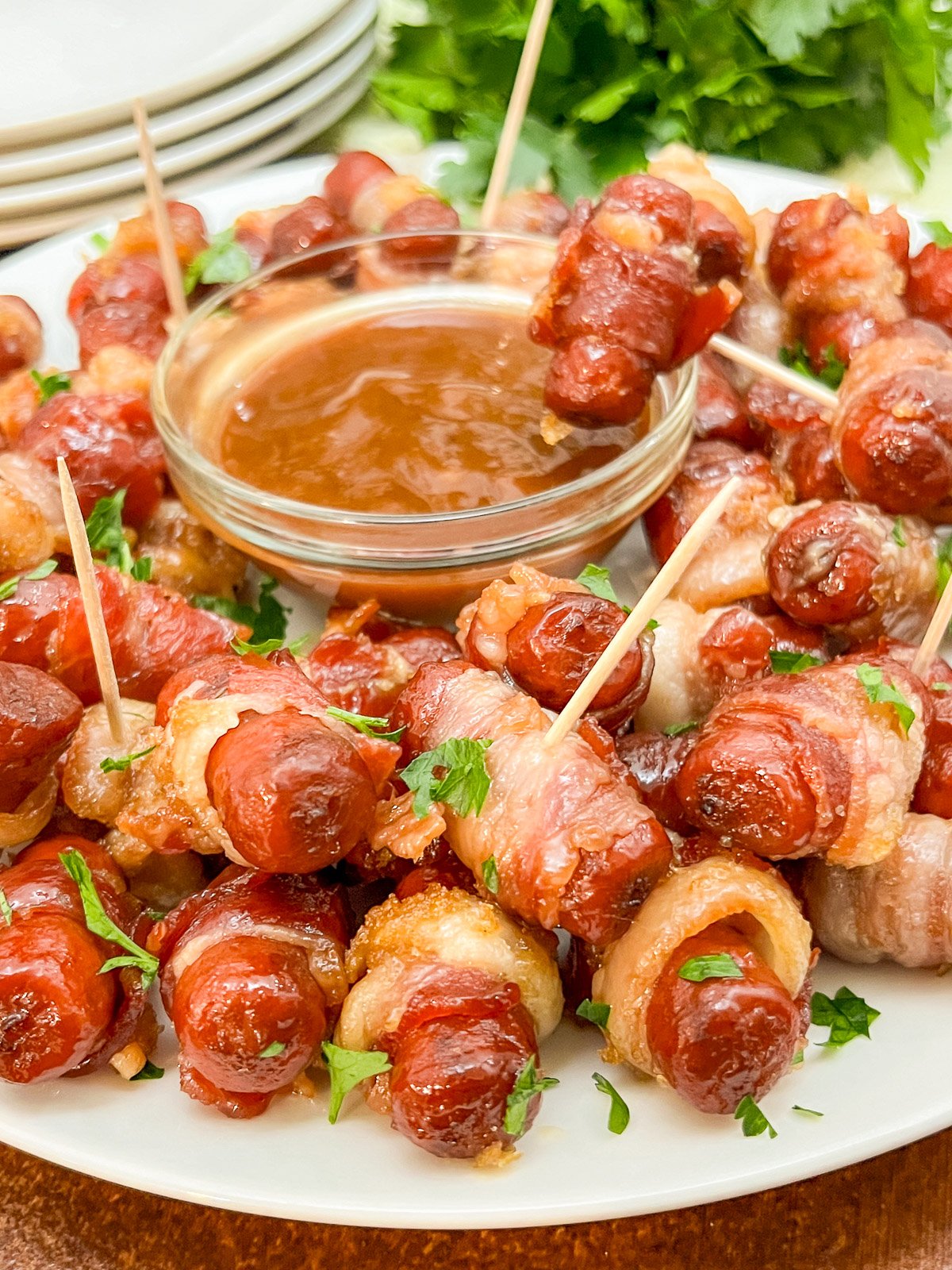 Bacon wrapped smokies piled on a platter around a bowl of BBQ dipping sauce.