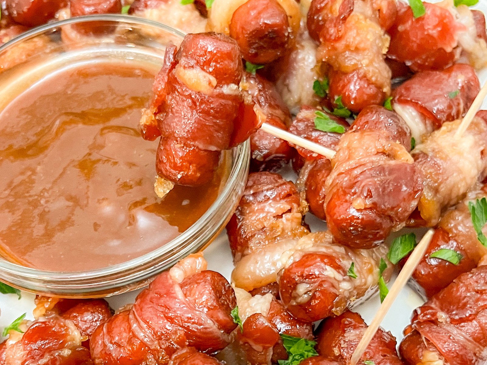 A bacon wrapped smokie being dipped into BBQ sauce.