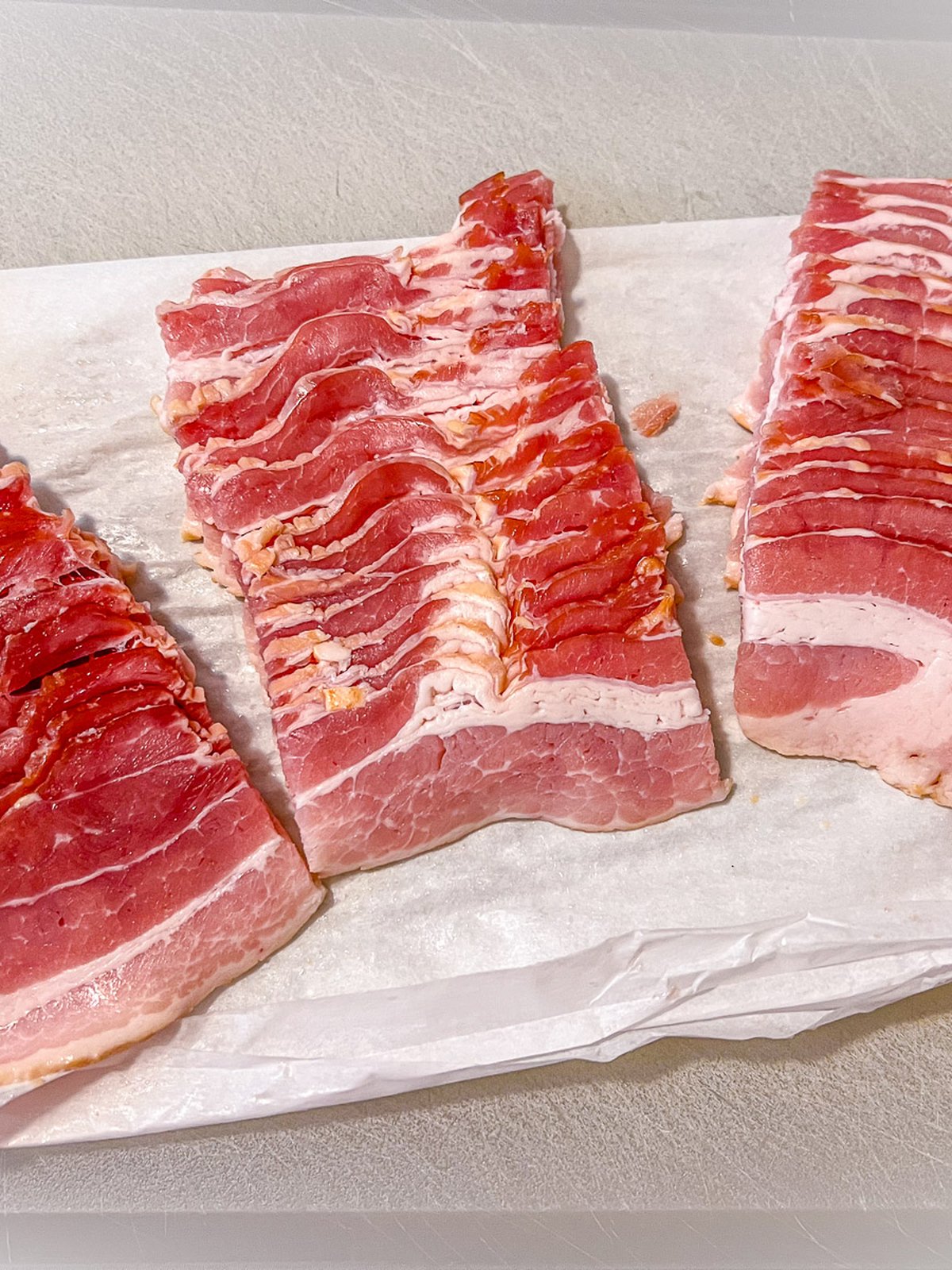 Bacon slices cut into thirds on parchment paper.