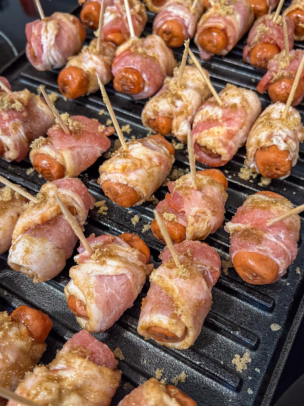 Bacon wrapped smokies arranged on a cast iron grill grate before baking.