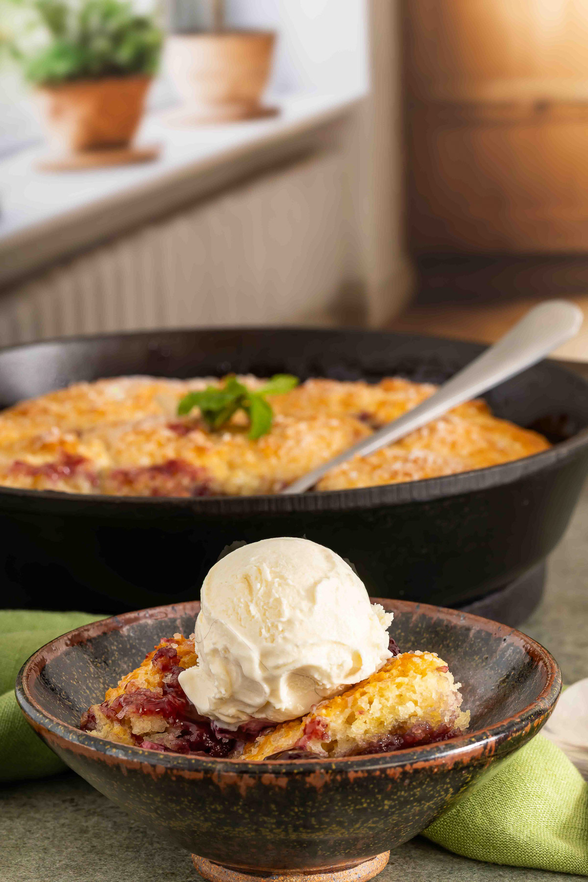 Cherry cobbler served with vanilla ice cream beside a cast iron skillet