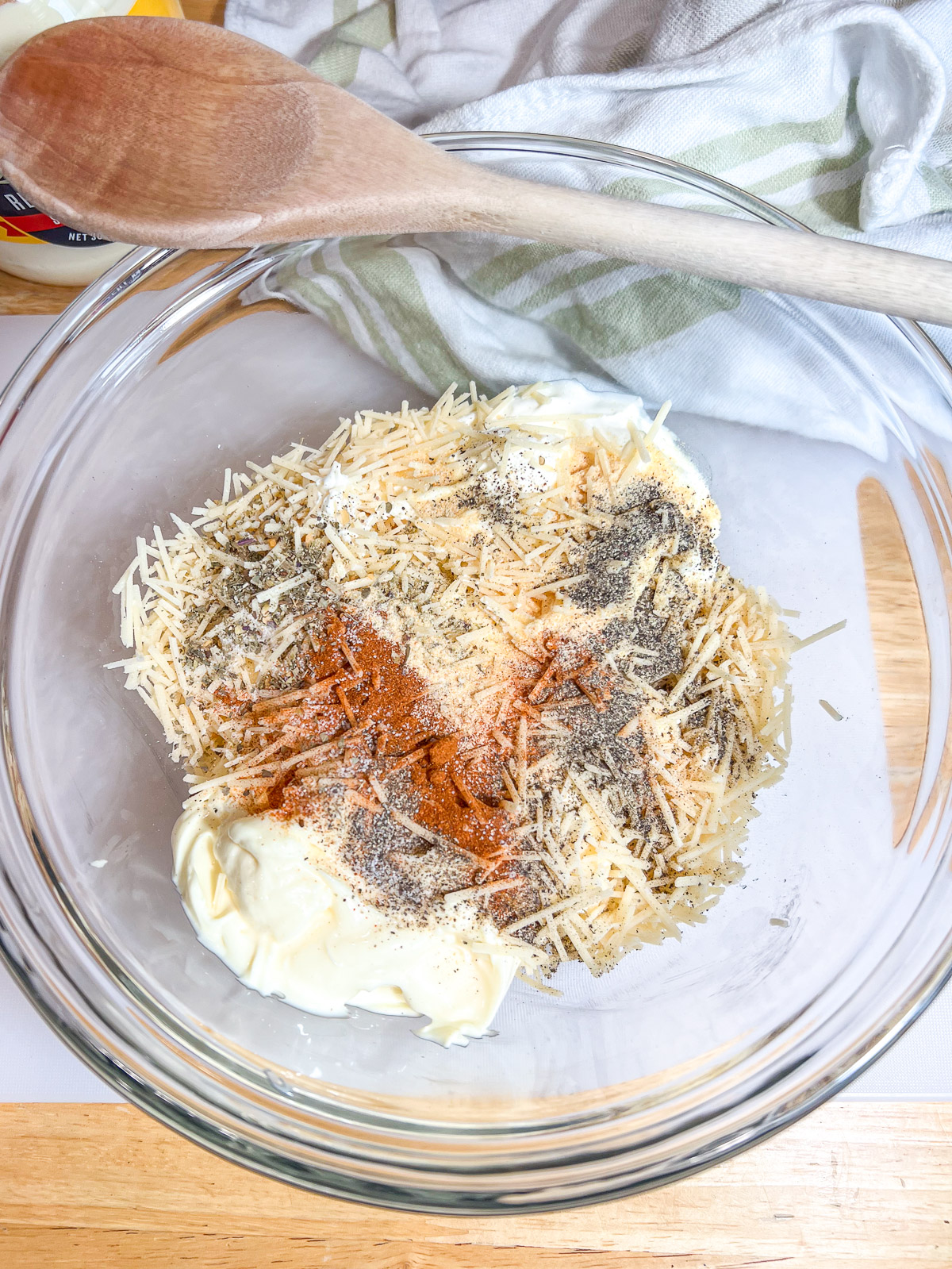 Cream cheese base topped with Parmesan, paprika, and seasonings in a glass bowl.