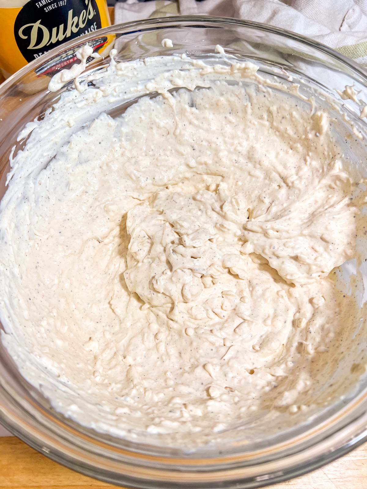 Creamy hot artichoke dip base whisked smooth in a glass bowl.