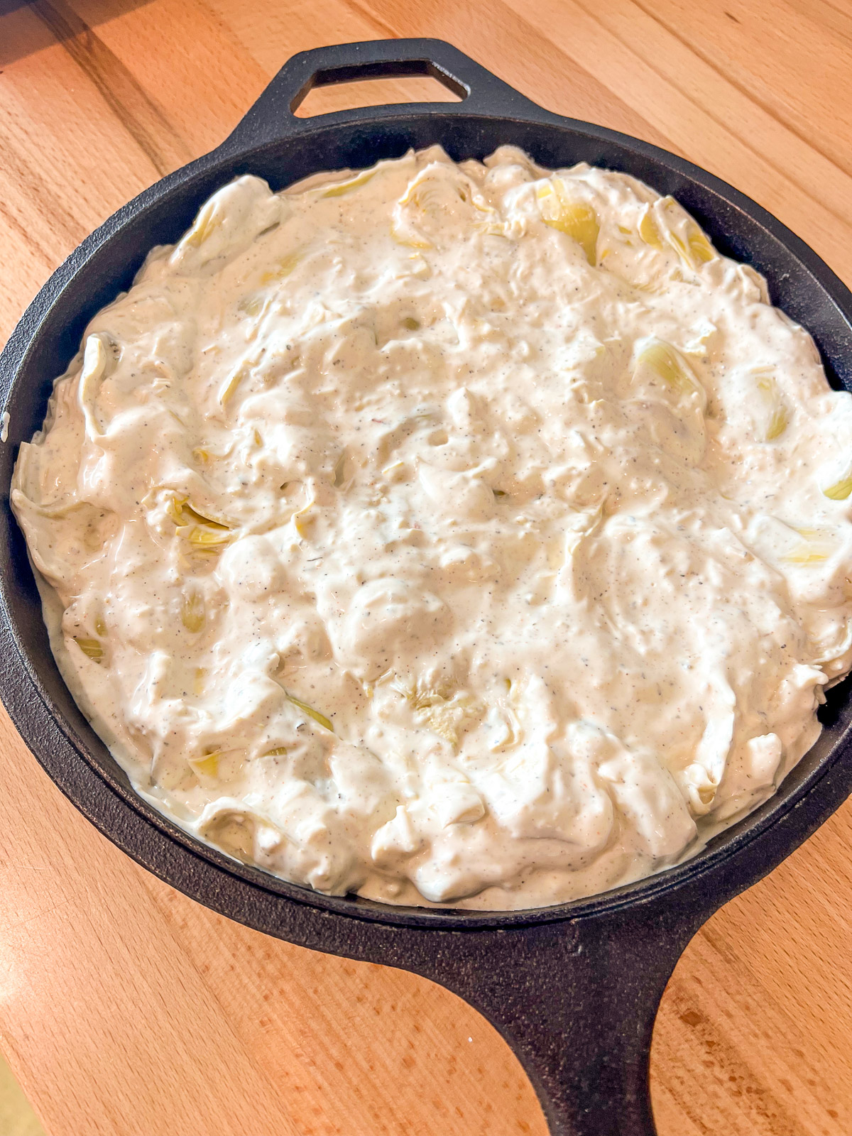 Hot artichoke dip spread into a cast iron skillet.