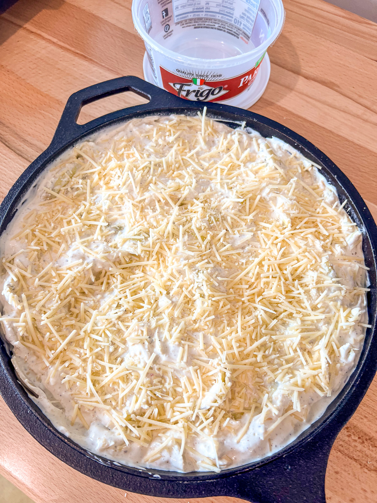 Shredded Parmesan sprinkled over the dip in a cast iron skillet.