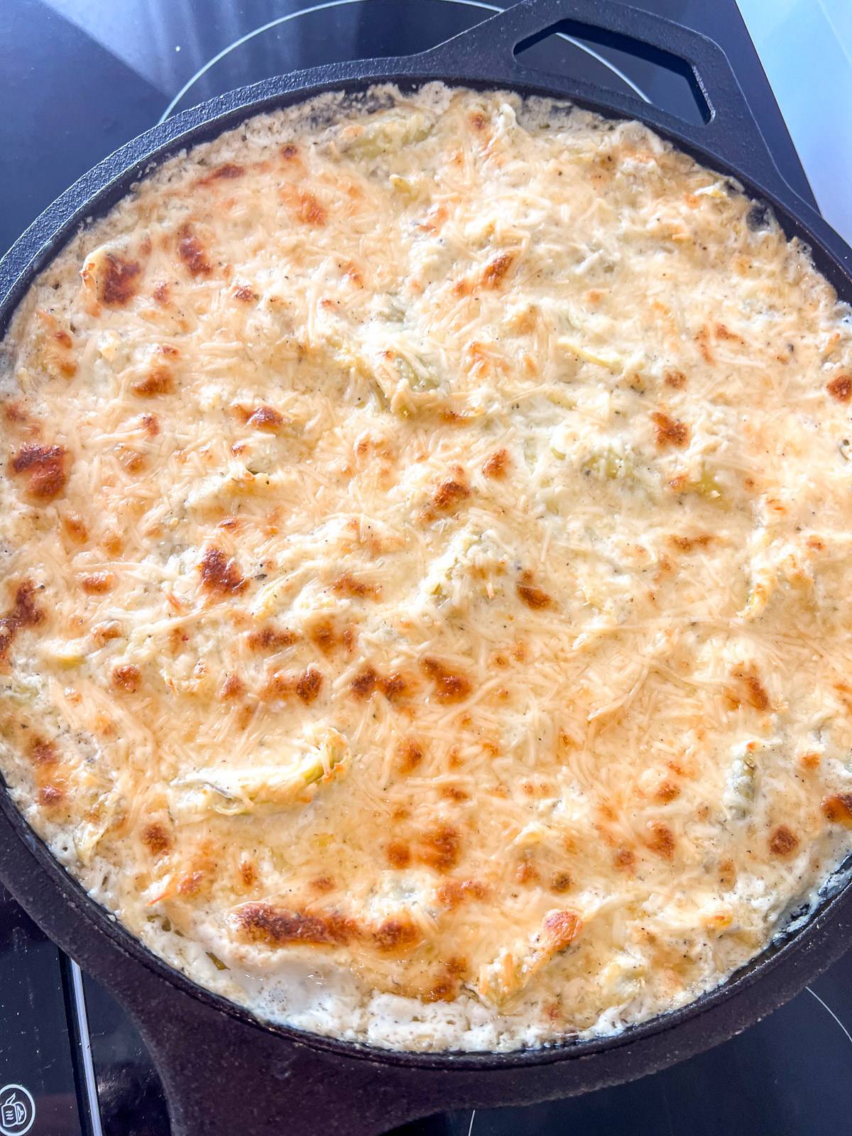 Golden, bubbly baked hot artichoke dip in a cast iron skillet.