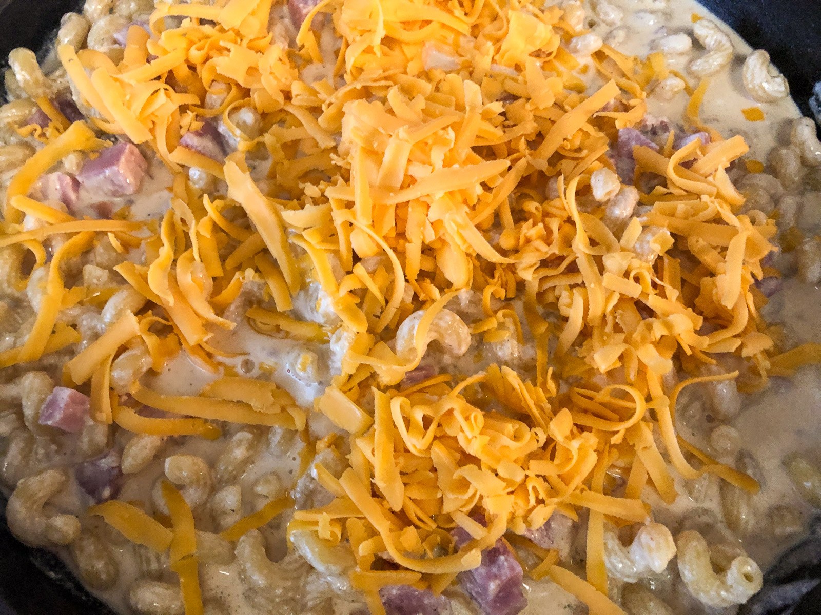 Grated cheddar cheese folded into the skillet mac and cheese with ham