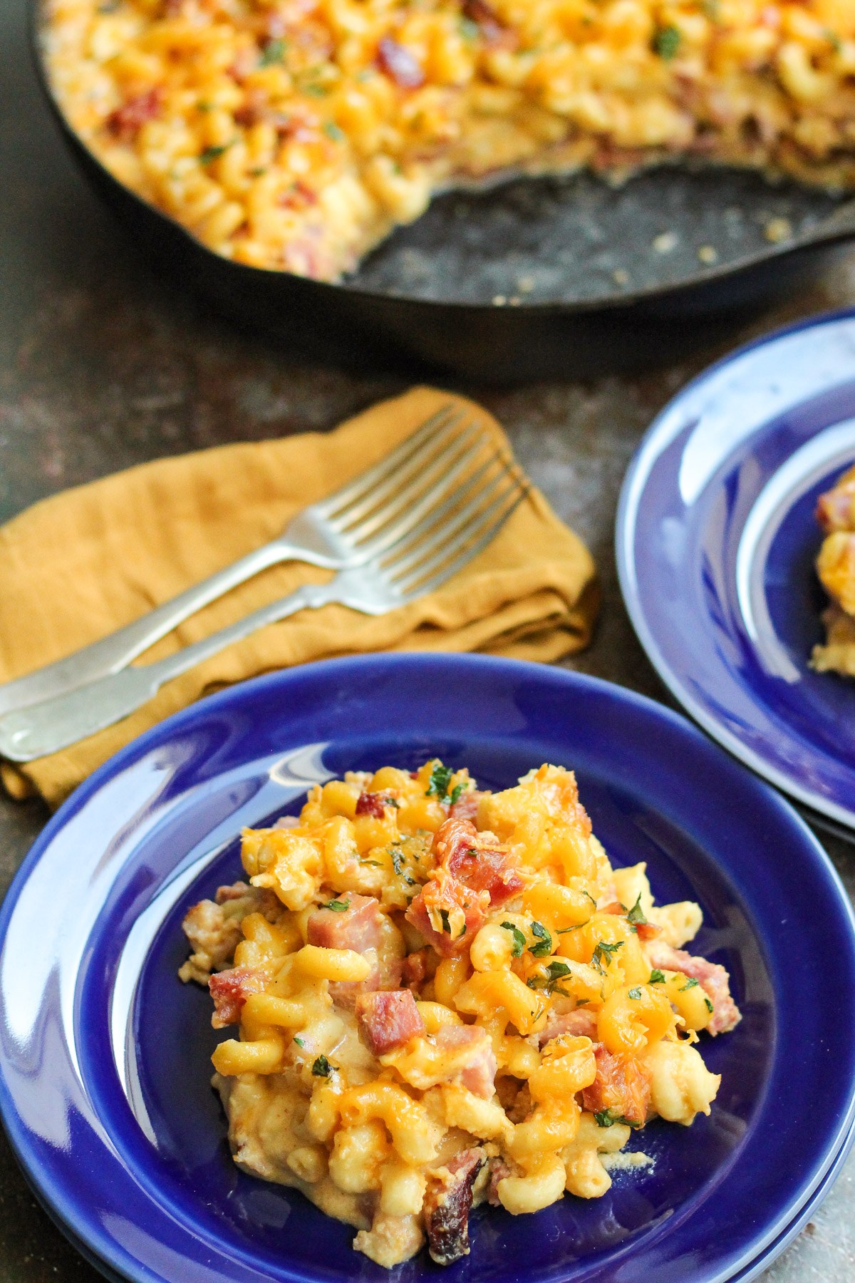 Skillet mac and cheese with ham on a blue plate with the cast iron skillet behind