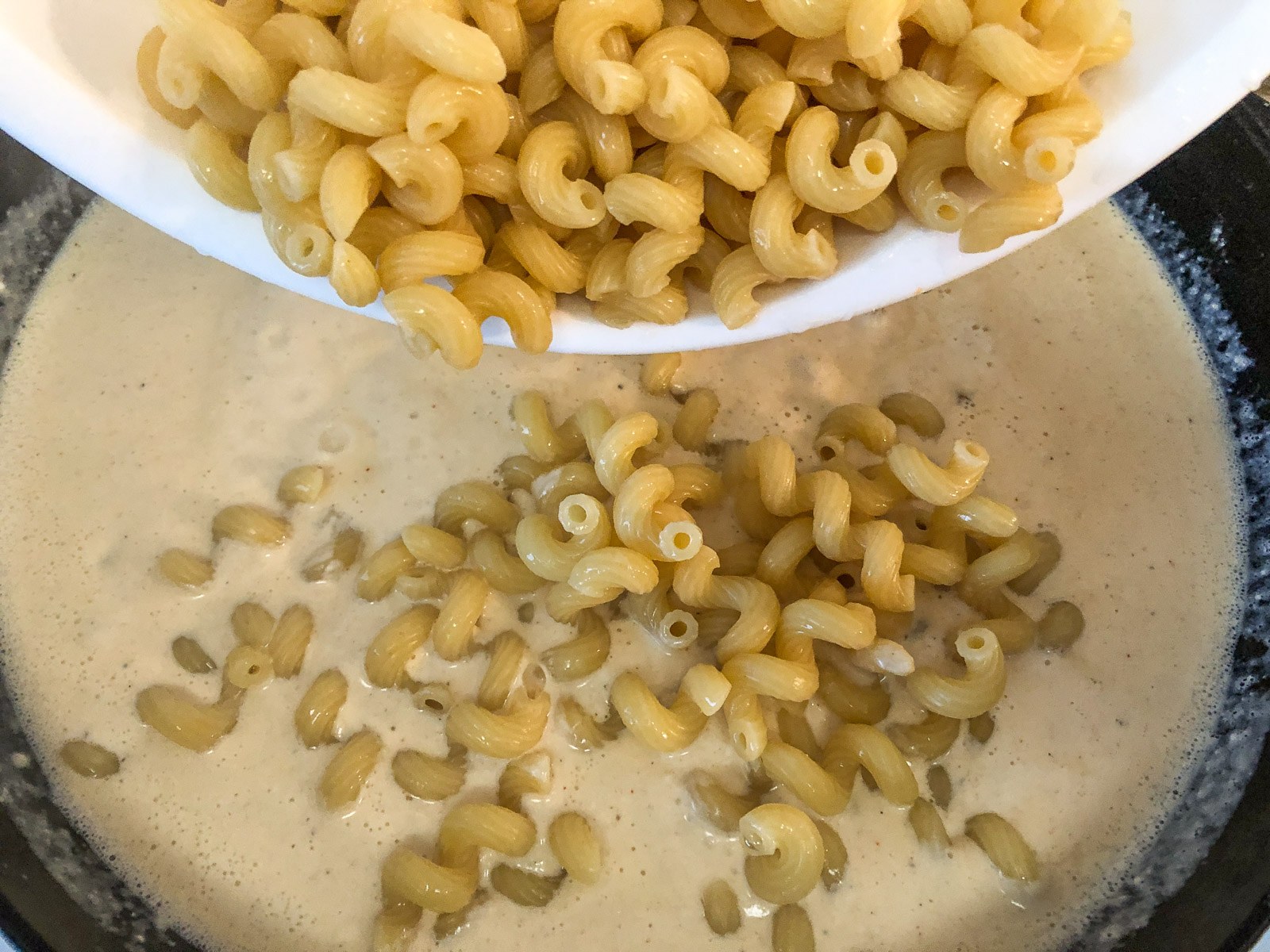 Cooked macaroni added to the creamy cheese sauce in the skillet
