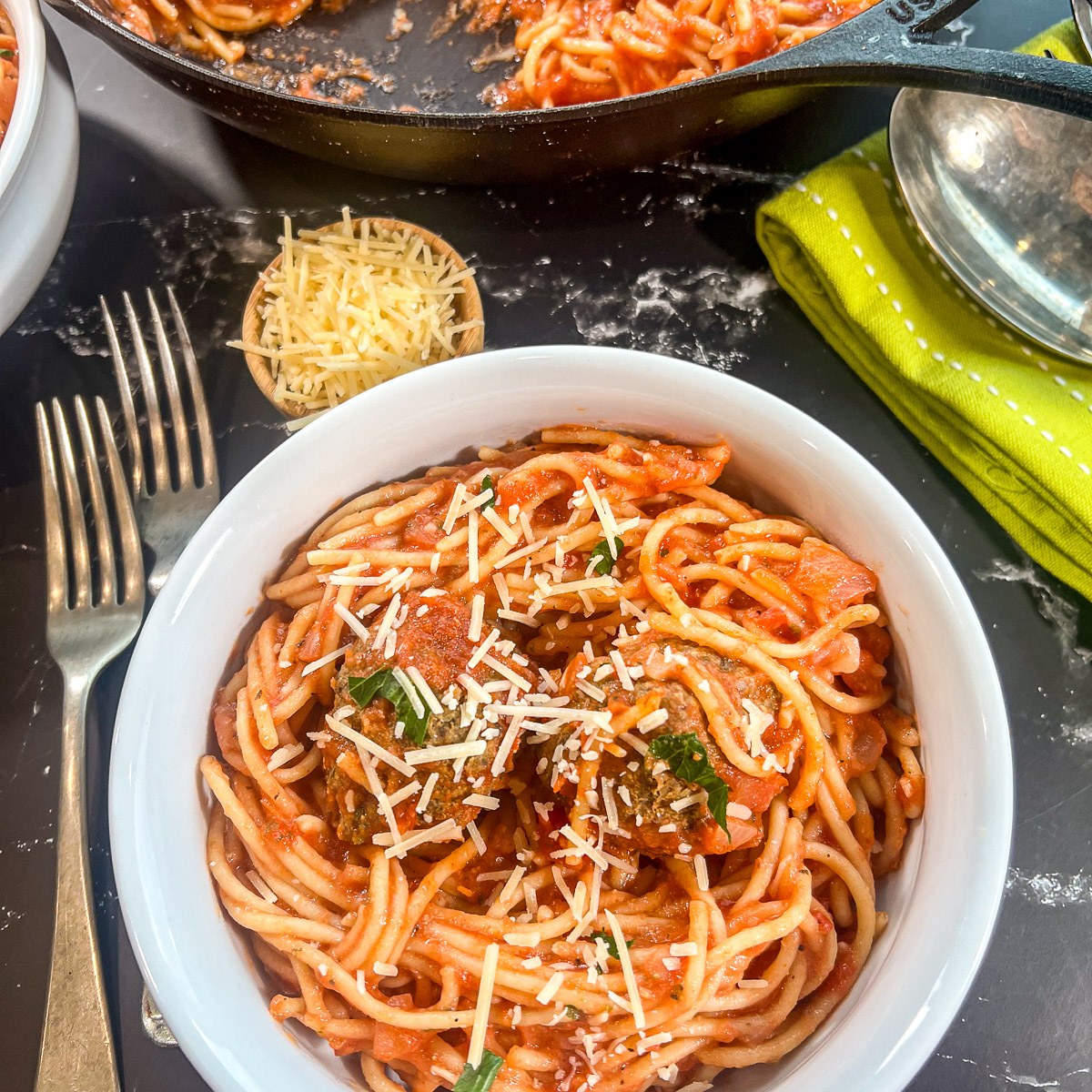 A white bowl of one pot spaghetti and meatballs garnished with Parmesan cheese.