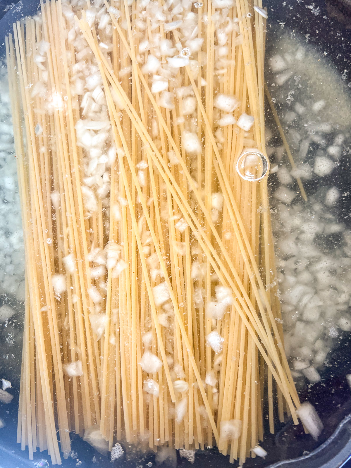 Uncooked spaghetti added to a cast iron skillet with water to cook in one pot.