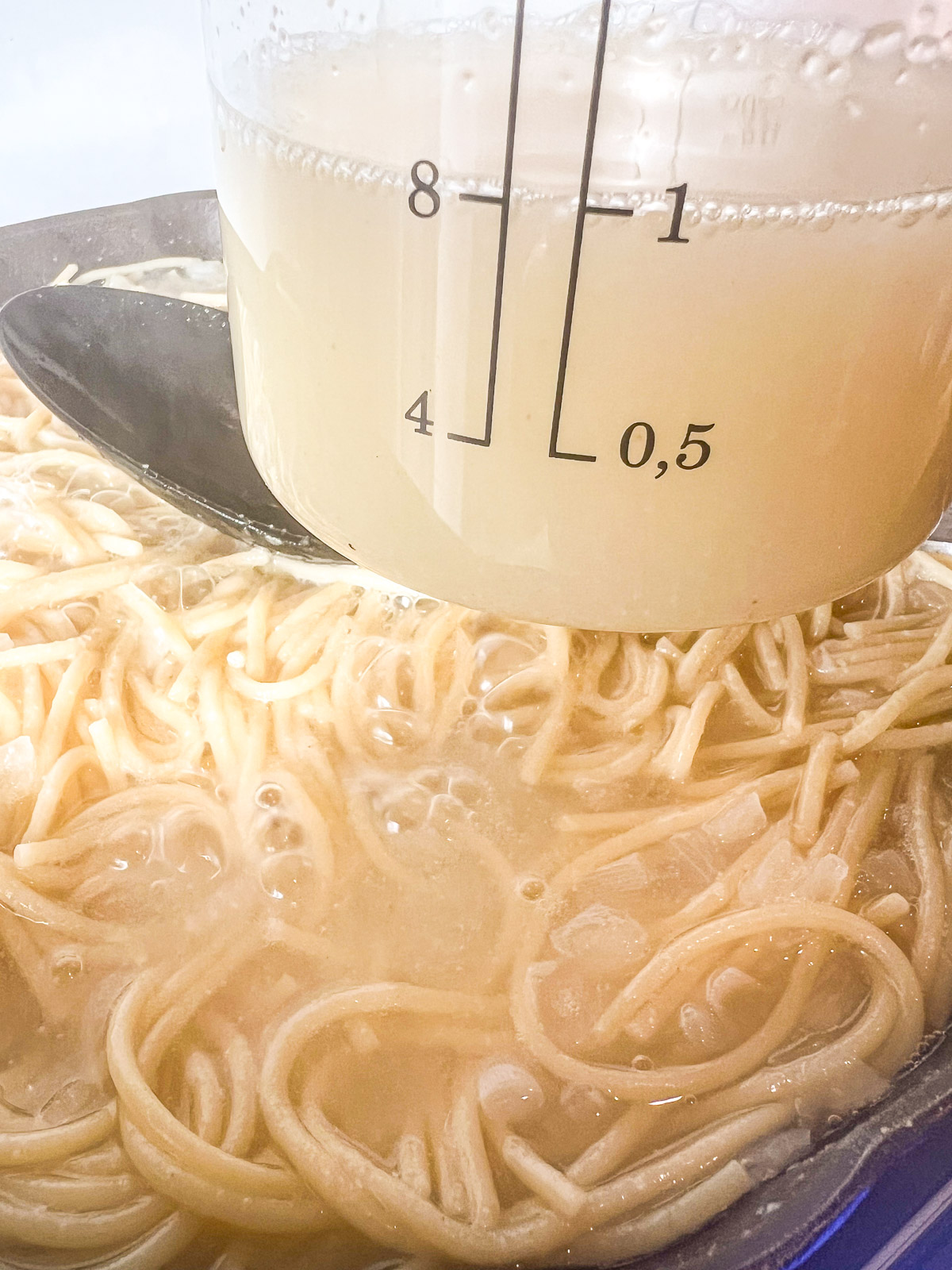 Reserving a cup of starchy pasta water from the cooked spaghetti in the skillet.
