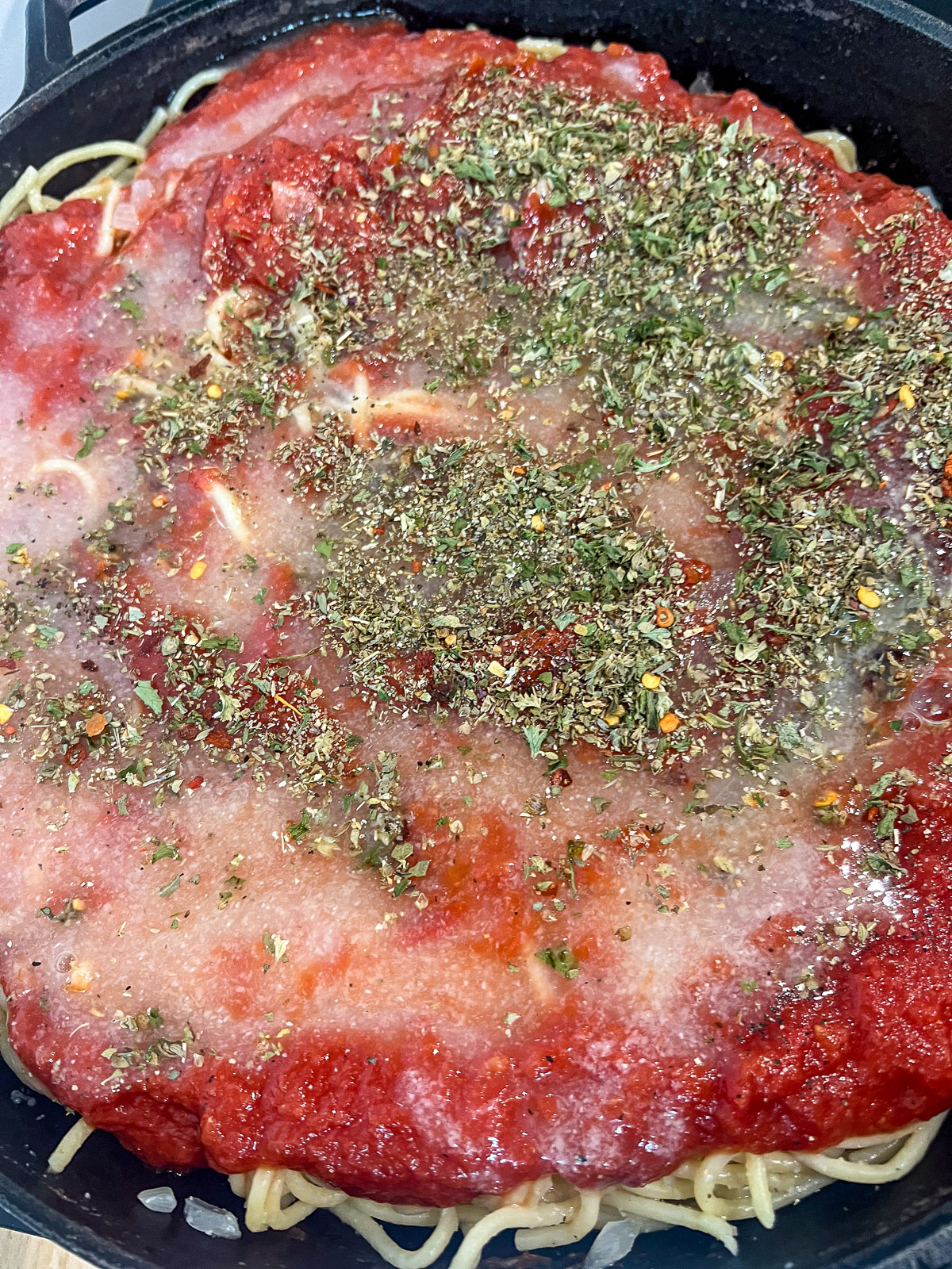 Crushed tomatoes and Italian seasonings added over the spaghetti in the skillet.