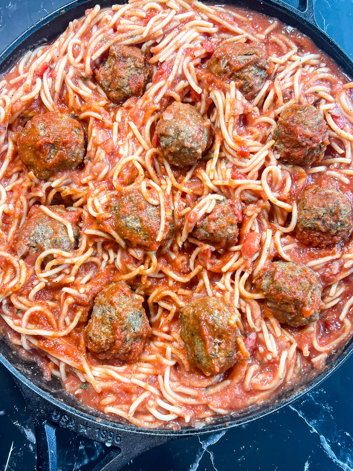 Meatballs stirred into the saucy spaghetti in the cast iron skillet.