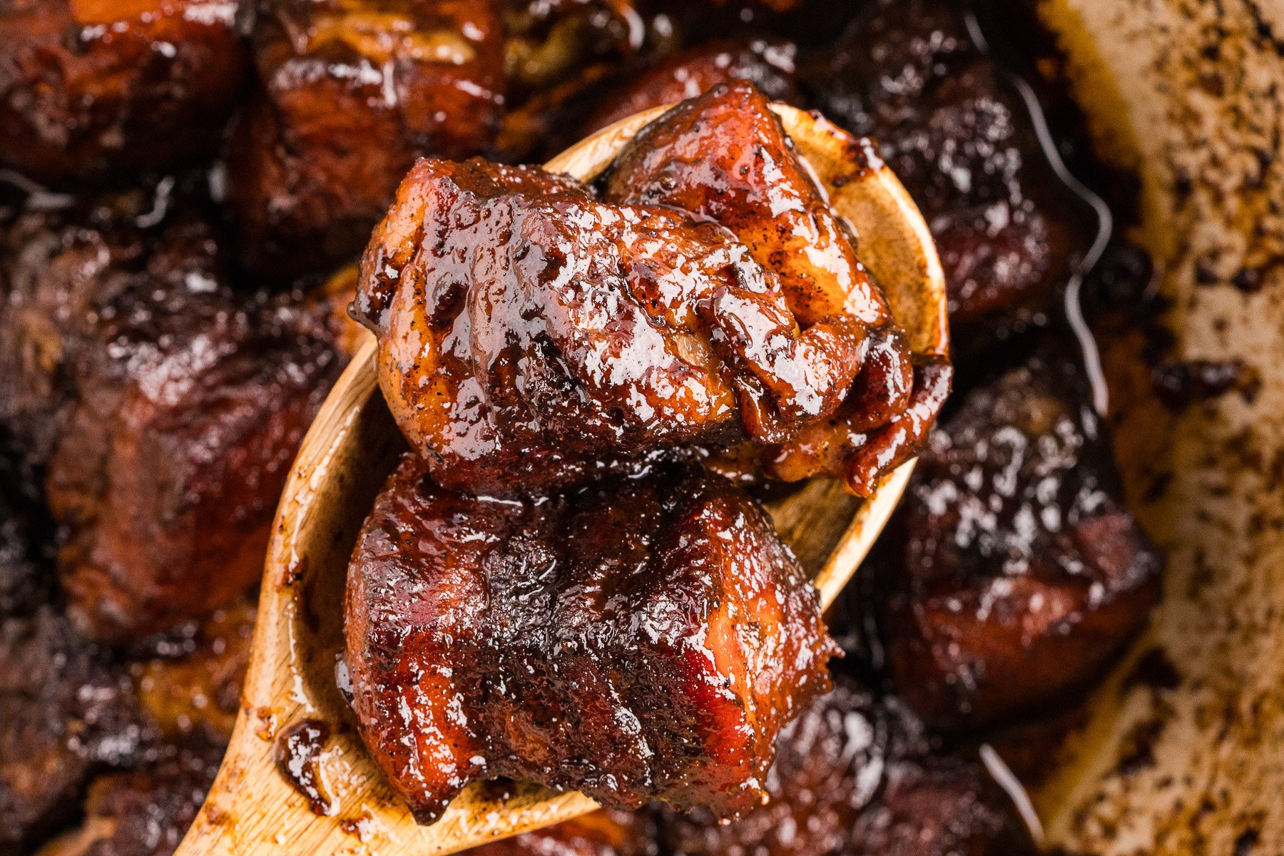 Stack of sticky pork belly burnt ends lifted on a serving spoon