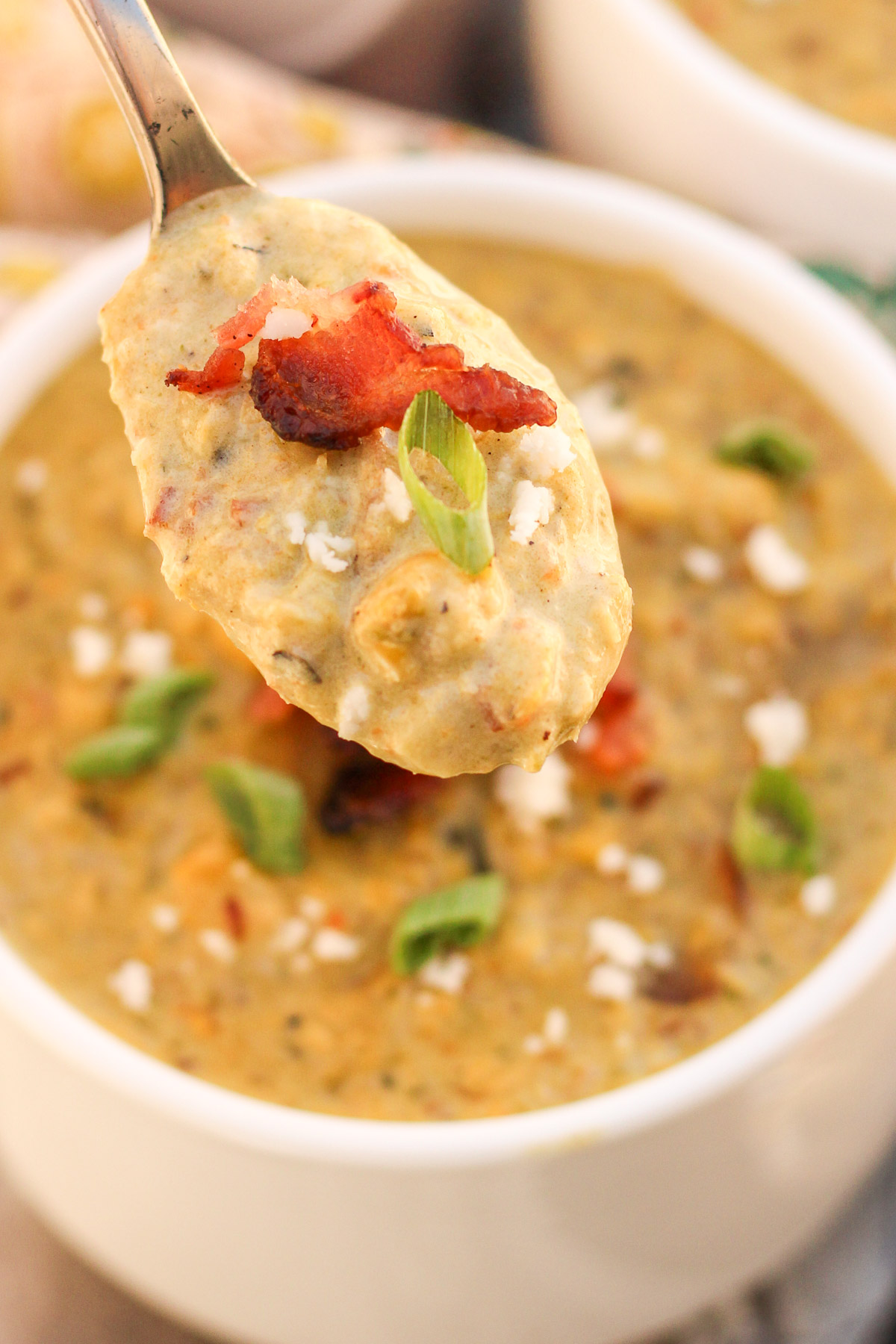 A spoonful of Roasted Poblano Corn Chowder raised above a white bowl.