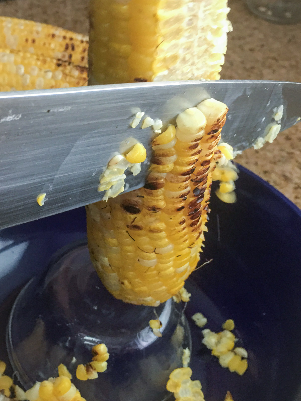 Roasted corn kernels being cut from the cob into a bowl.