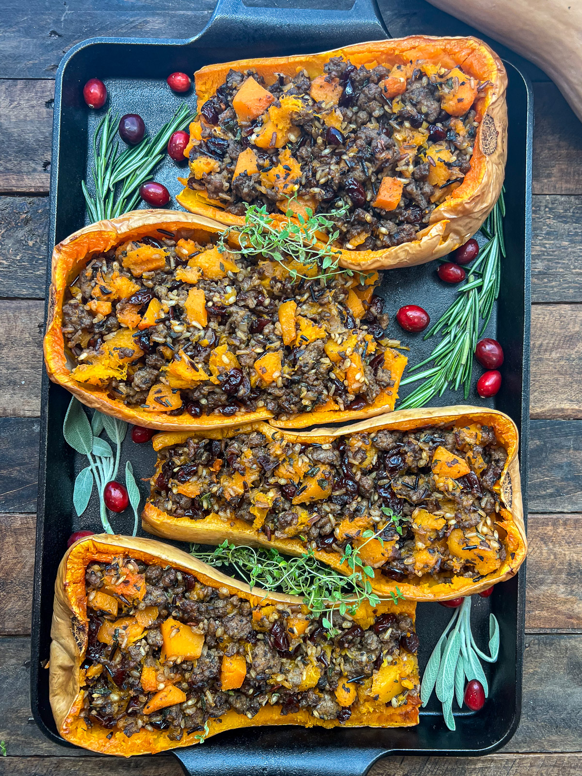 Sausage stuffed butternut squash garnished with sage and cranberries in a cast iron pan.