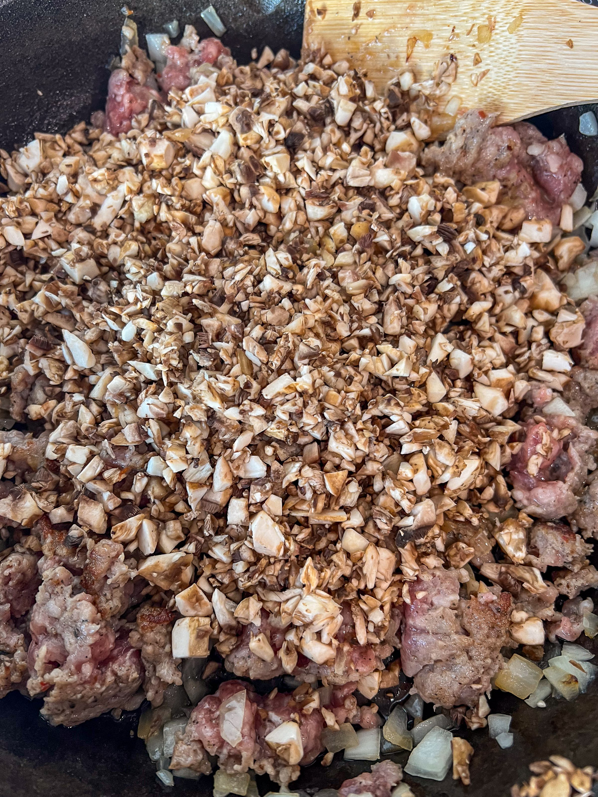 Diced button mushrooms added to the sausage and onion in the skillet.