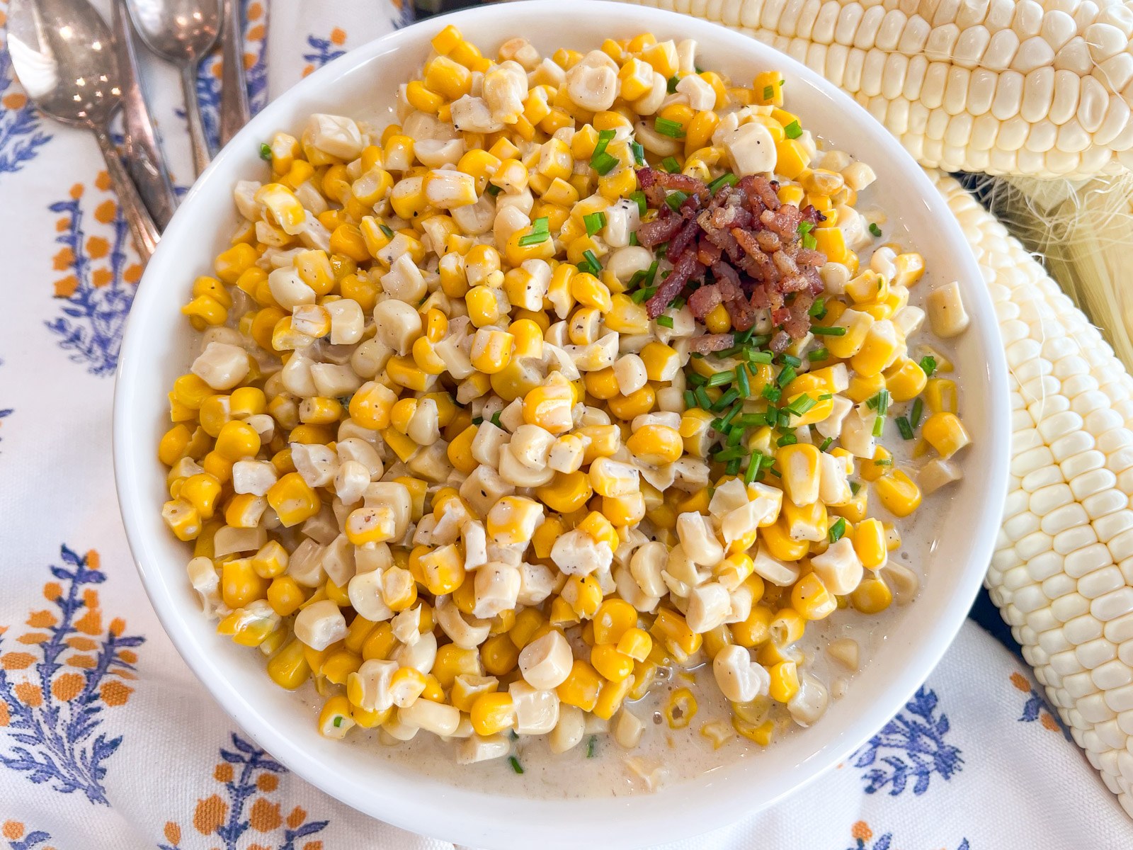 Southern creamed corn served in a white bowl with fresh corn on the cob.