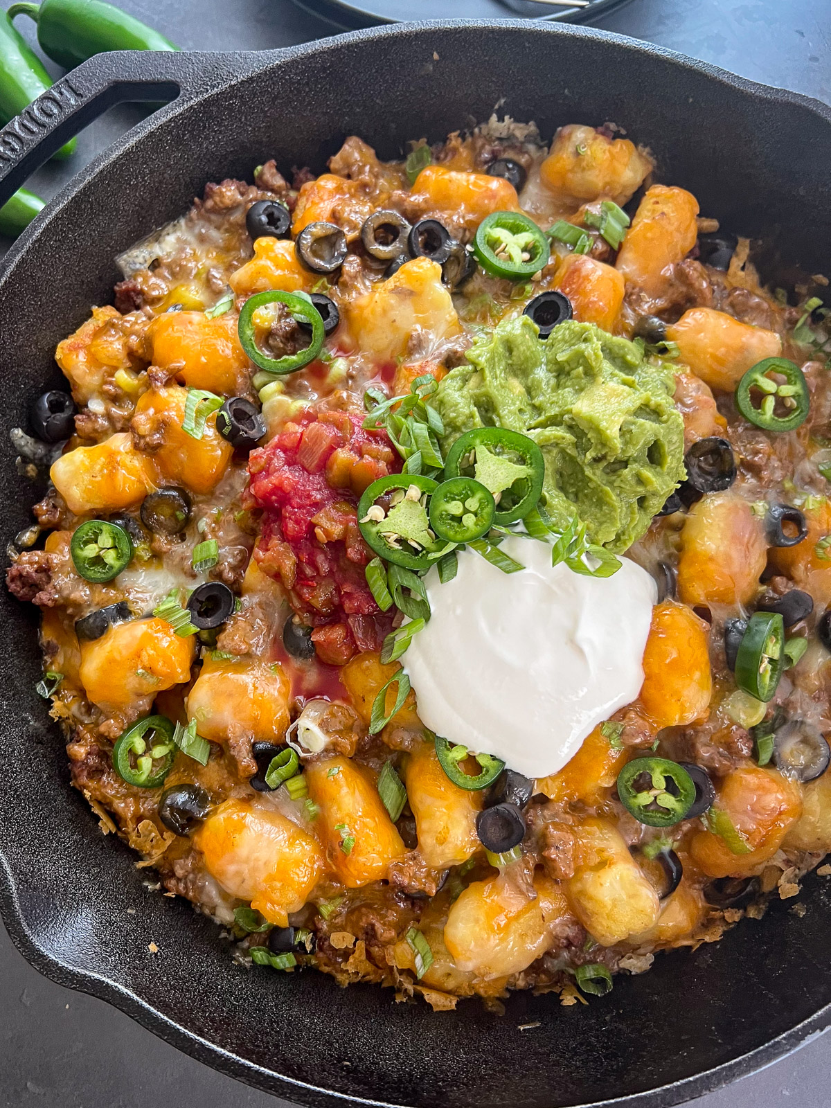 Loaded tater tot nachos (totchos) in a cast iron skillet topped with sour cream, salsa, jalapenos, and green onions.