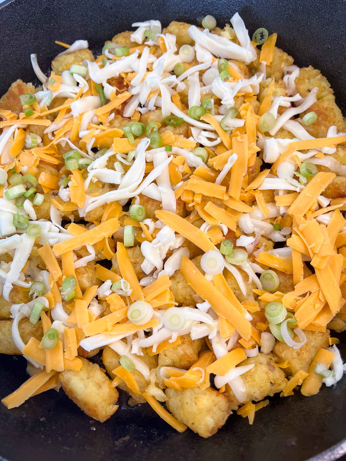 First layer of tater tots topped with shredded cheese in a cast iron skillet.