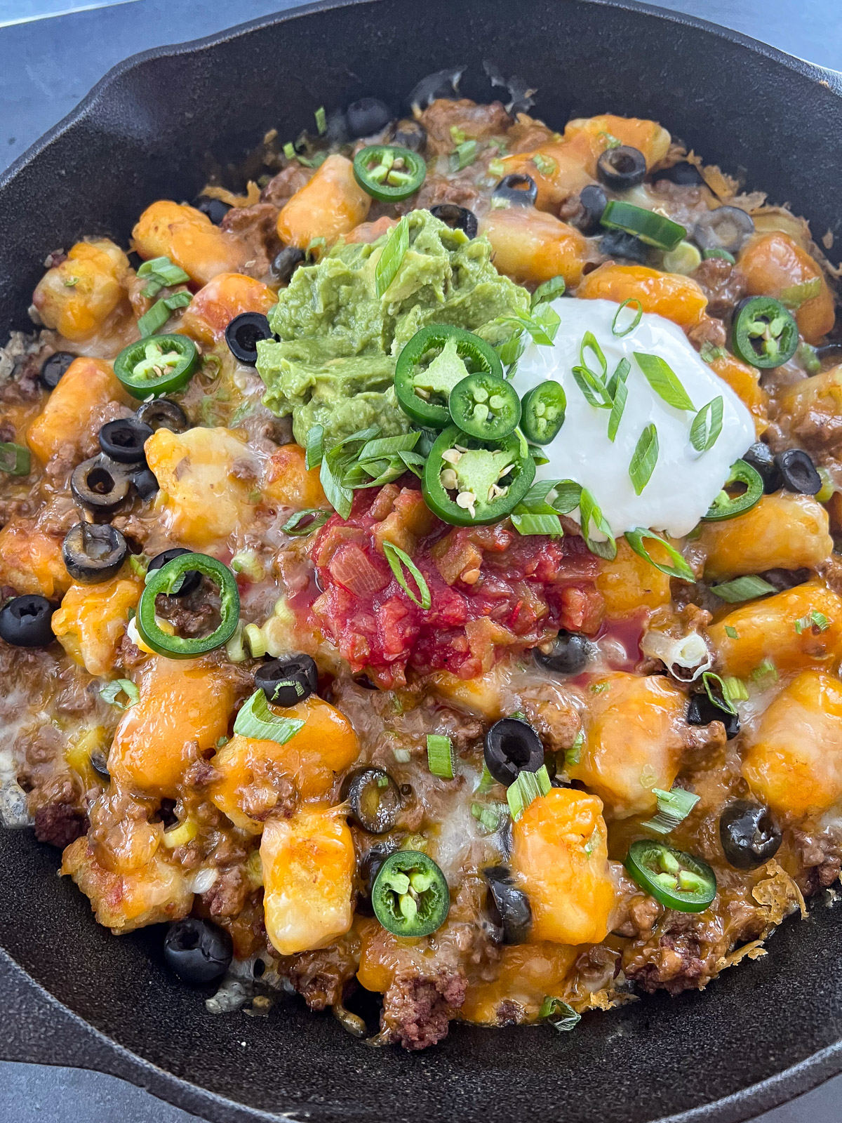 Finished tater tot nachos garnished with sour cream, jalapenos, and green onions.