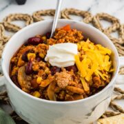 Bowl of vegetable turkey chili topped with shredded cheddar and sour cream