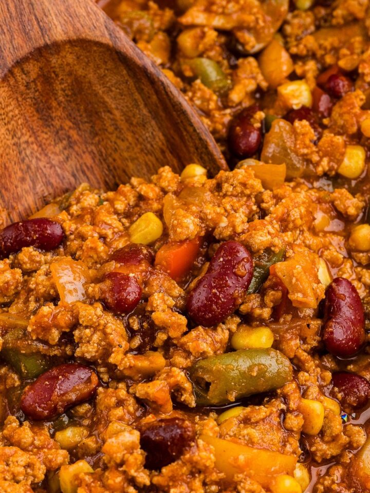 Wooden spoon lifting vegetable turkey chili from a cast iron Dutch oven
