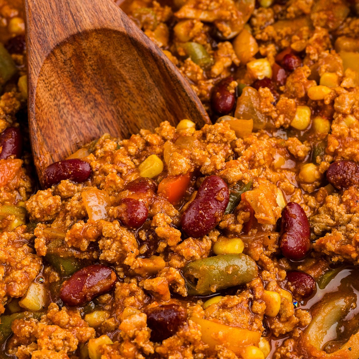 Wooden spoon lifting vegetable turkey chili from a cast iron Dutch oven