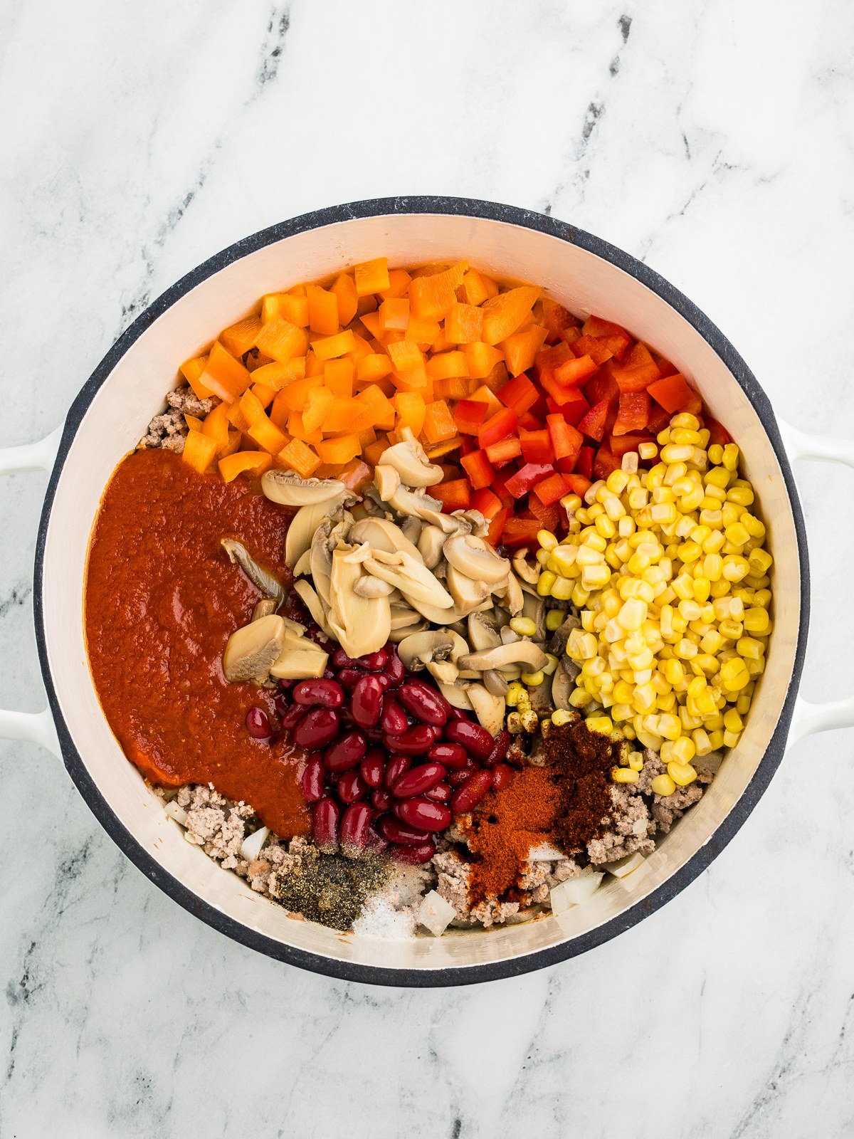 Adding sauce, beans, corn, peppers and mushrooms