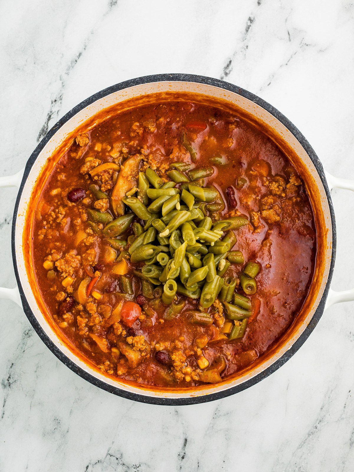 Stirring green beans into the simmering chili
