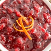 Top down view of homemade cranberry sauce with an orange twist garnish in a white bowl.