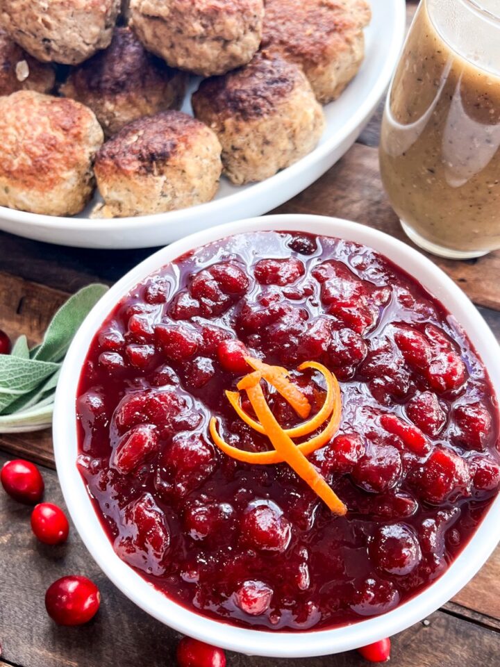 Homemade cranberry sauce with orange in a white bowl on a holiday table with turkey meatballs and gravy.