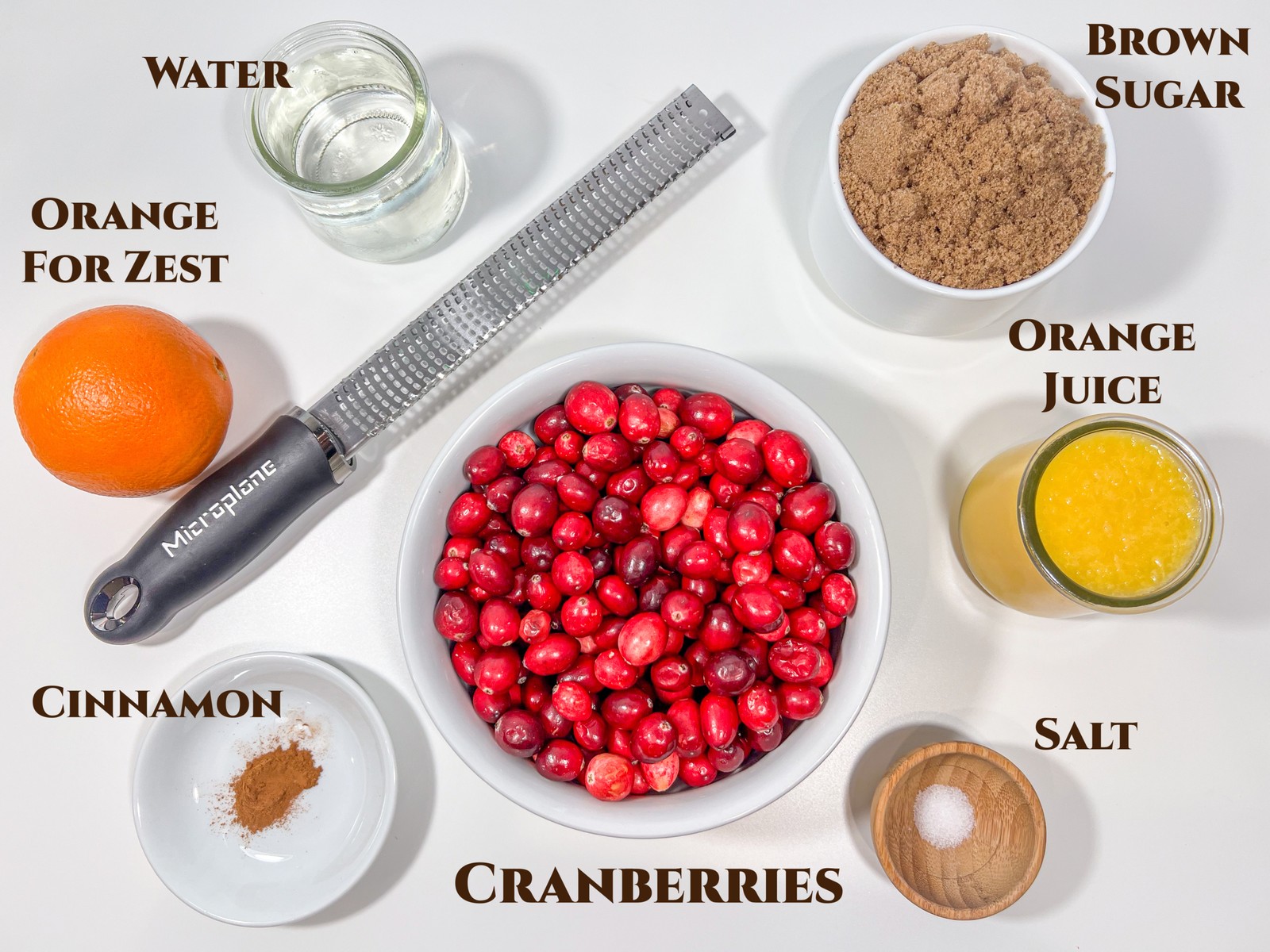 Ingredients for homemade cranberry sauce: fresh cranberries, an orange, dark brown sugar, orange juice, water, cinnamon, and salt.