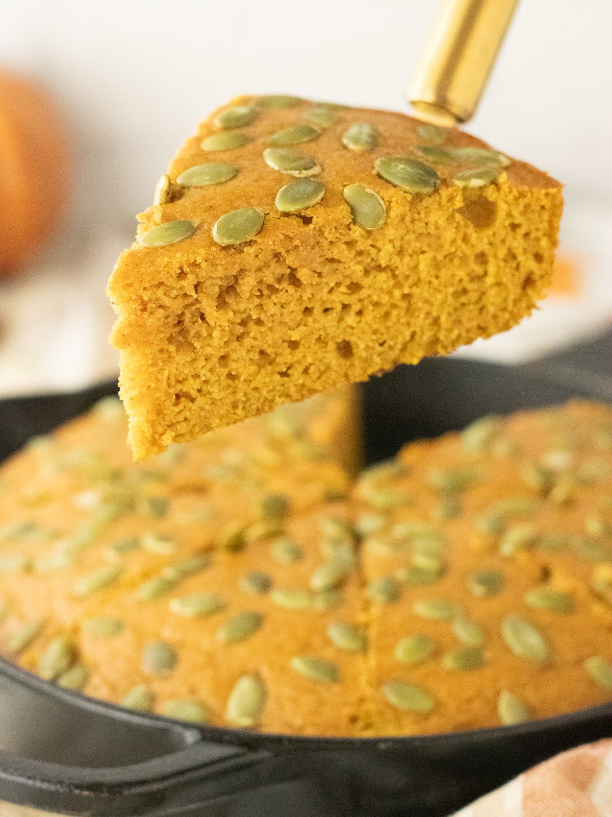 A slice of pumpkin cornbread lifted from the skillet showing the moist golden crumb
